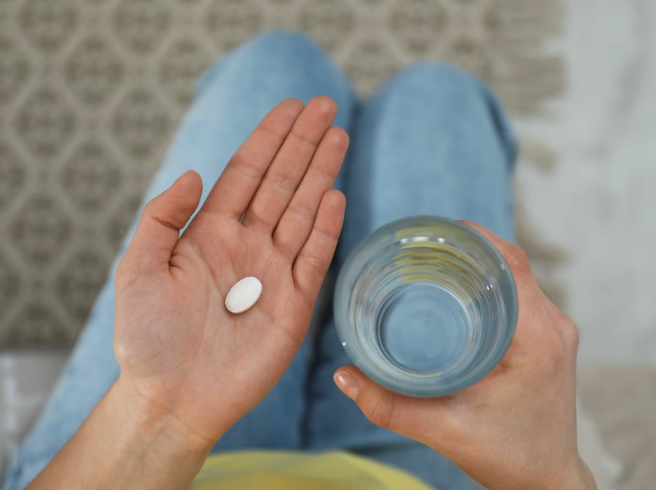 Woman holding abortion pill and glass of water, wearing blue jeans and yellow shirt