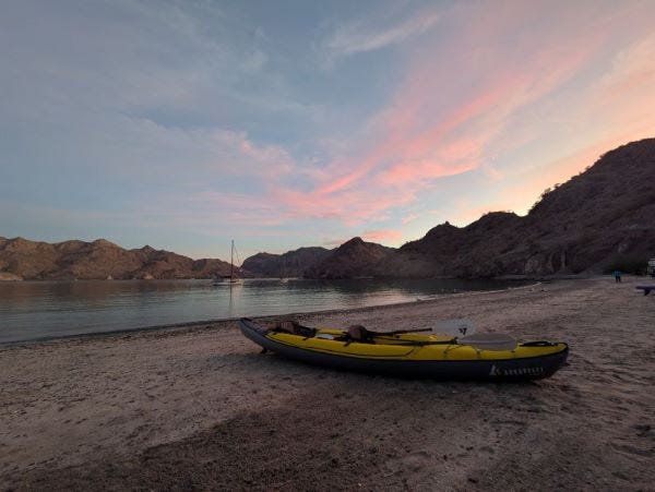 a yellow inflatable kayak on a beach at sunset with pink streaking through the sky