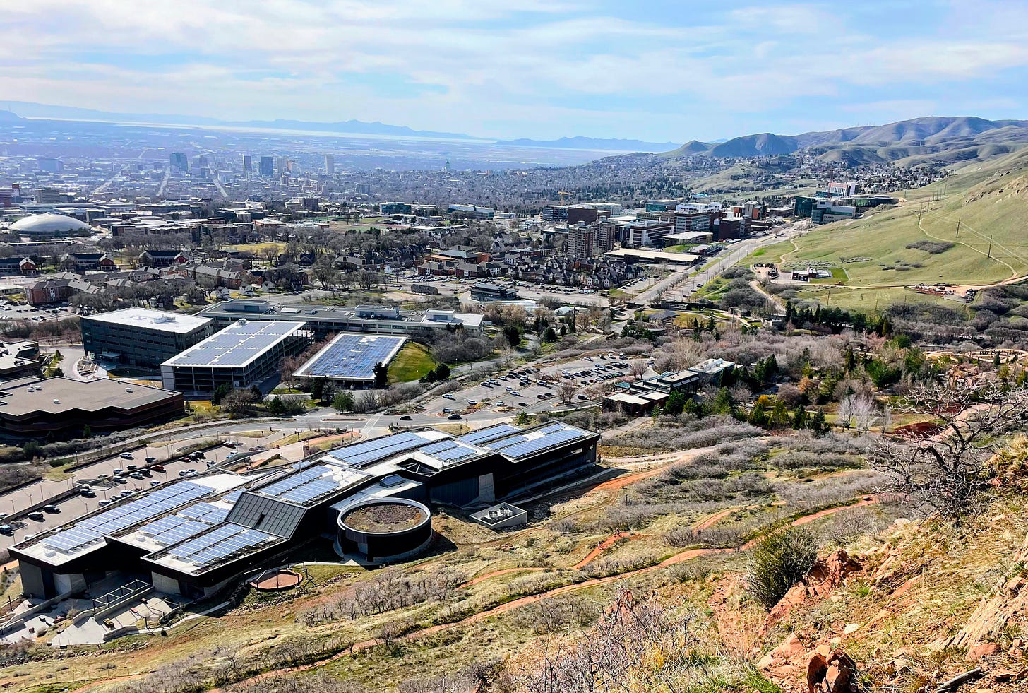 A view of Salt Lake City from the foothills east of the city. In the foreground a number of large buildings are topped with large arrays of solar panels.