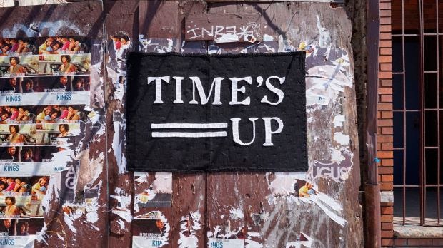 A picture of a knitted panel pinned to a wall. The knitted banner reads "Times Up"