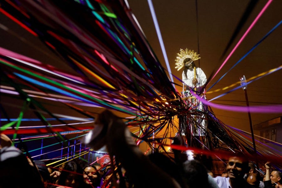 People gather beneath a statue of Jesus Christ, entangled in many colorful ribbons.