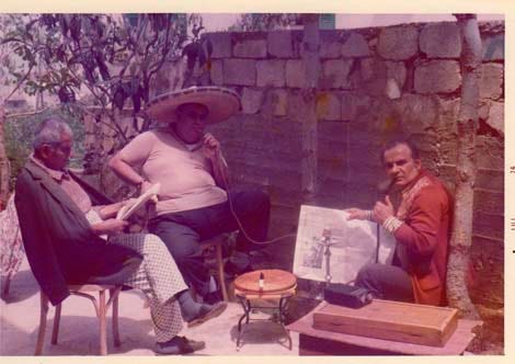 A photo taken in the late 1970s, by the author, of his father, grandfather and uncle, sitting around a hookah, two reading newspapers. In the near distance, a tree, and a wall of concrete blocks.