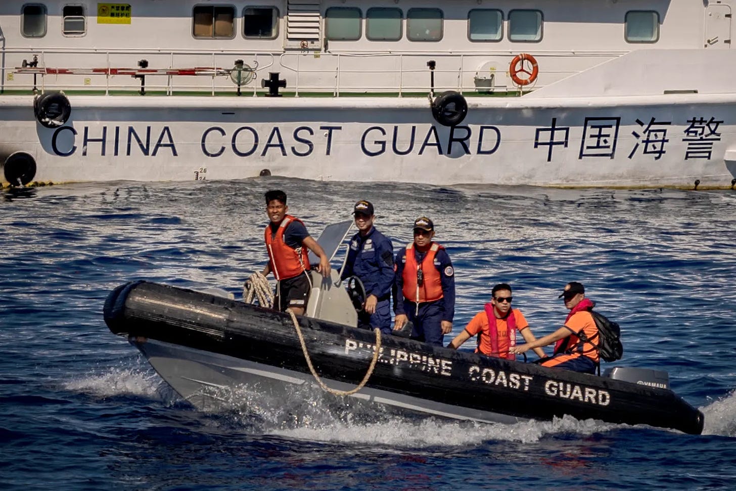 Philippine Coast Guard personnel ride a rubber boat past a China Coast Guard vessel in the South China Sea.