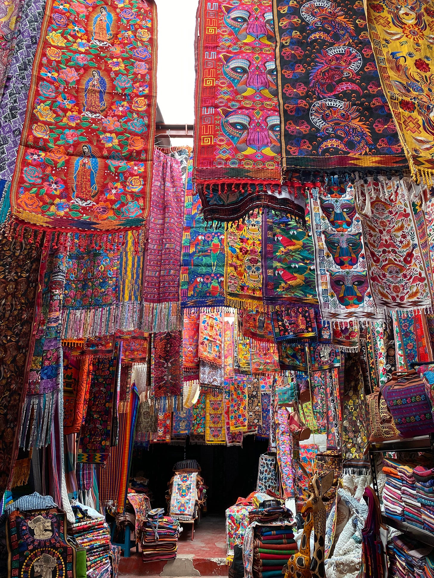 A store with a hanging display of bright, bold weavings and wall hangings.