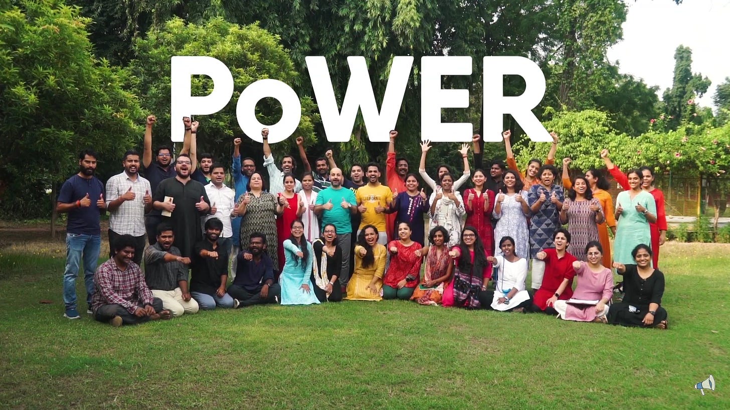 A large group of people posing for a picture in a garden/park. The background in the picture says- POWER in bold white font