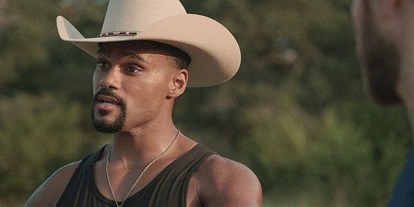 Trey in tank top and cowboy hat looking very drag Village People.