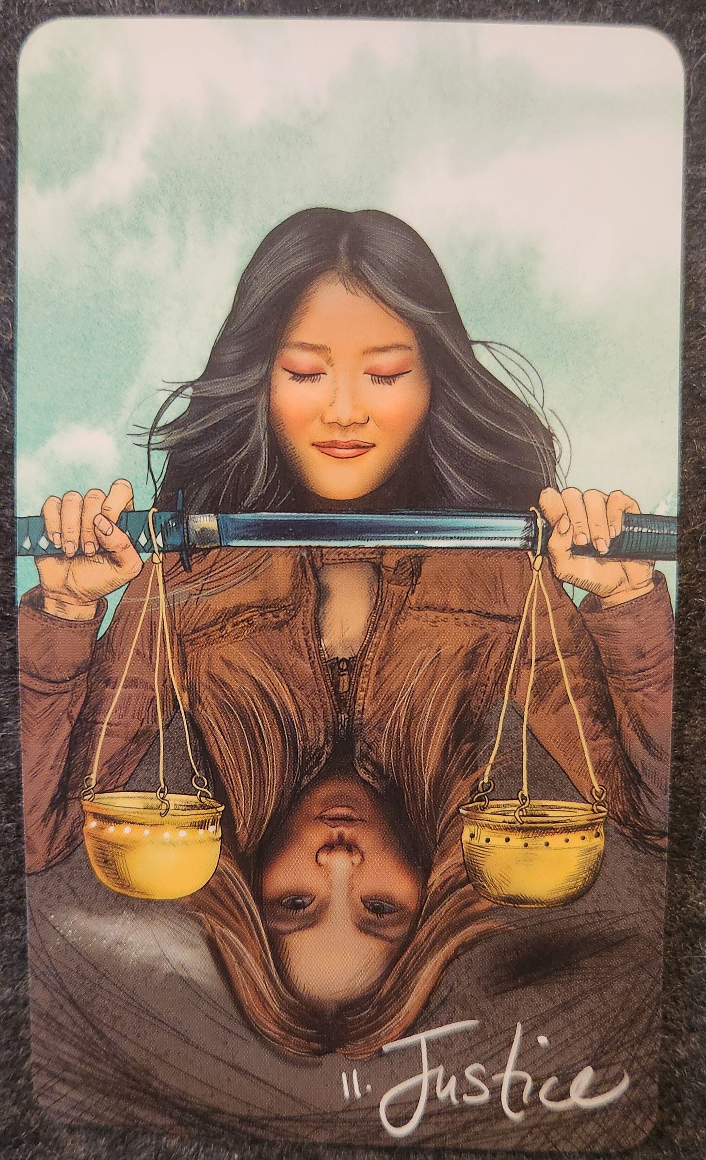 A tarot card labelled 10. Justice. A woman is holding a long sword upright in both hands. Her eyes are closed, her face is peaceful, a slight smile on her lips. Hanging from the sword is a set of balanced scales. Below the sword is a reflection of a similar looking woman with open eyes and lighter hair. 