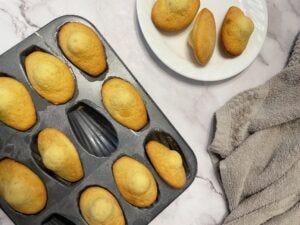 Madeleines in a madeleine mould and on a plate with a tea towel to the side.