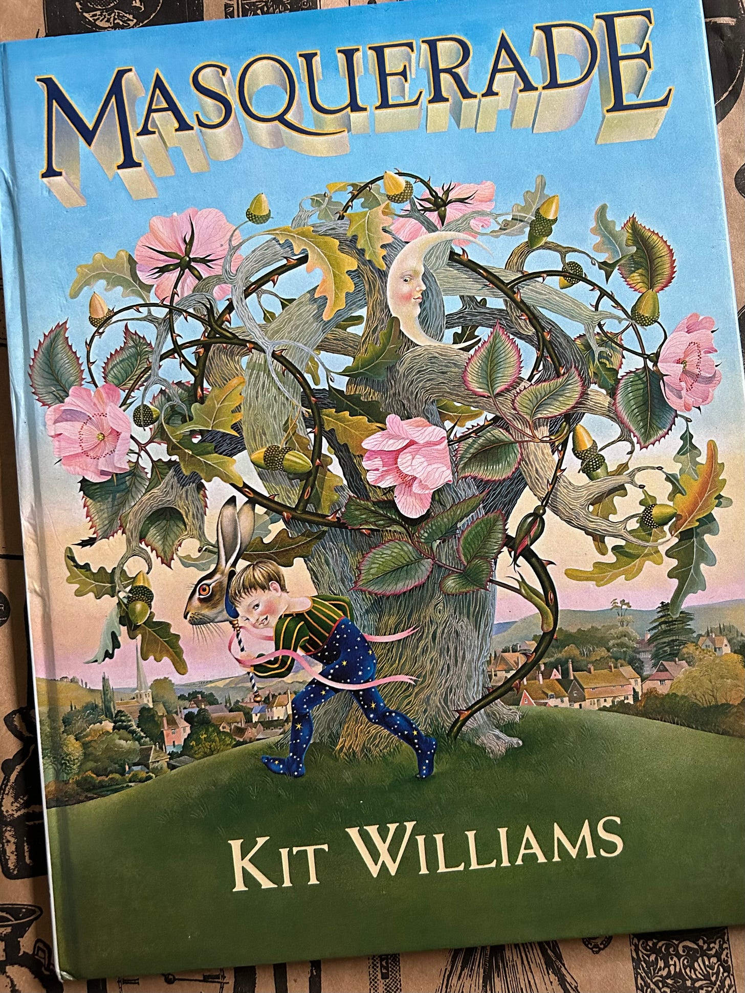 A copy of Masquerade by Kit Williams. The cover is highly coloured and shows a child dancing around a mystical tree, holding the head of a hare as a mask