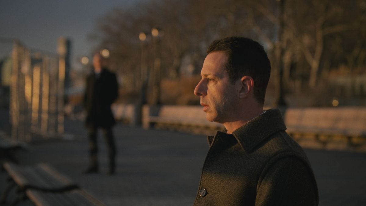 Kendall Roy staring out at the sea; in the background his father's bodguard -- now his -- stands out of focus