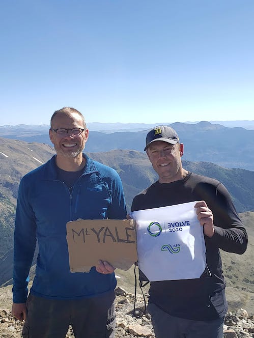 Two men holding signs on a mountain

Description automatically generated