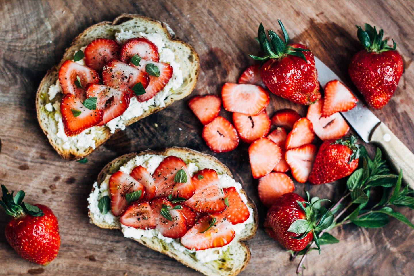 Sliced of strawberry ricotta toast on a cutting board with sliced strawberries alongside. 