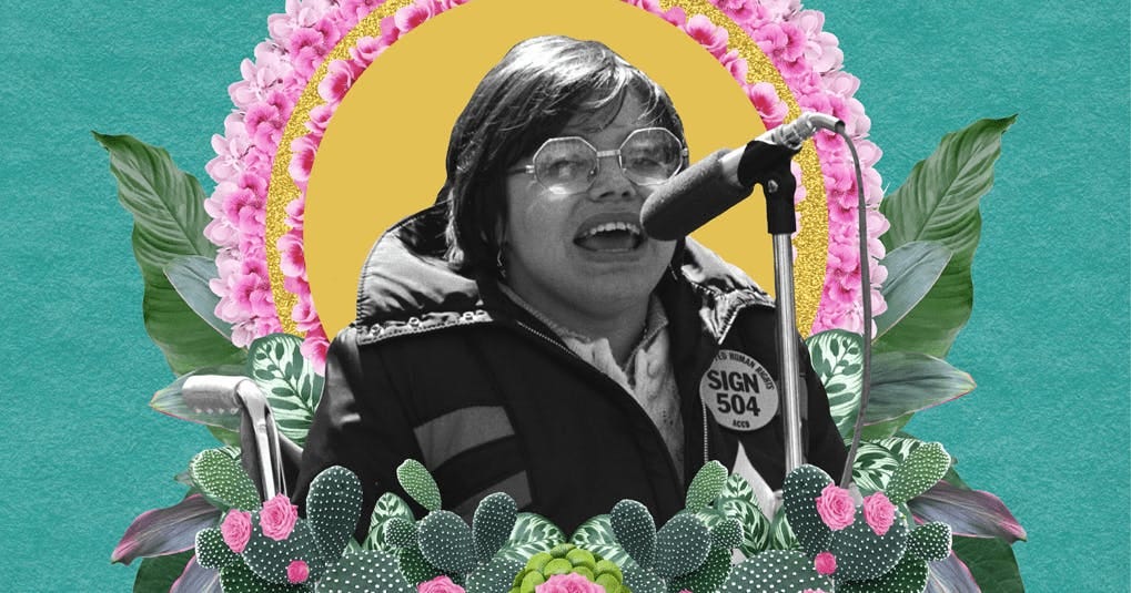 A white, wheelchair-using woman with glasses and short cropped hair is speaking into a mic on a sunny day. She wears a coat with a large button that says SIGN 504. This is a black and white photo that has been cropped. Around her are halos of pink flowers, green petals, and cacti.