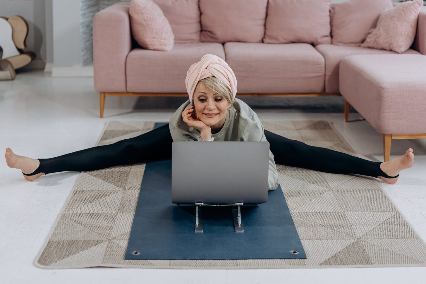 woman stretching on the floor while looking at her laptop
