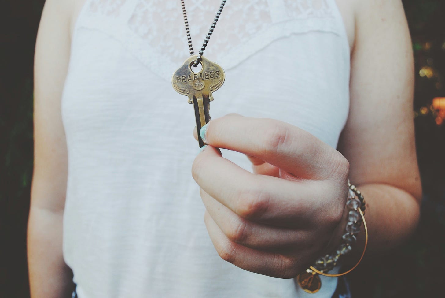 woman in a white sleeveless shirt with a key saying FEARLESS on a chain around her neck