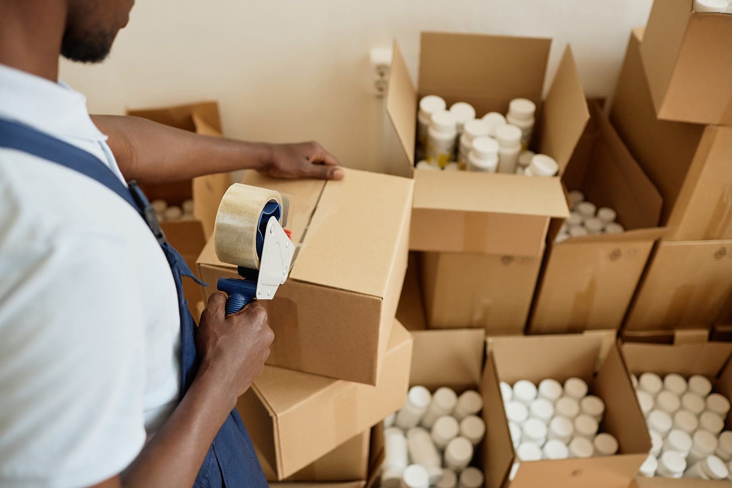 Close up of a young man sealing up boxes of medicine bottles for shipping