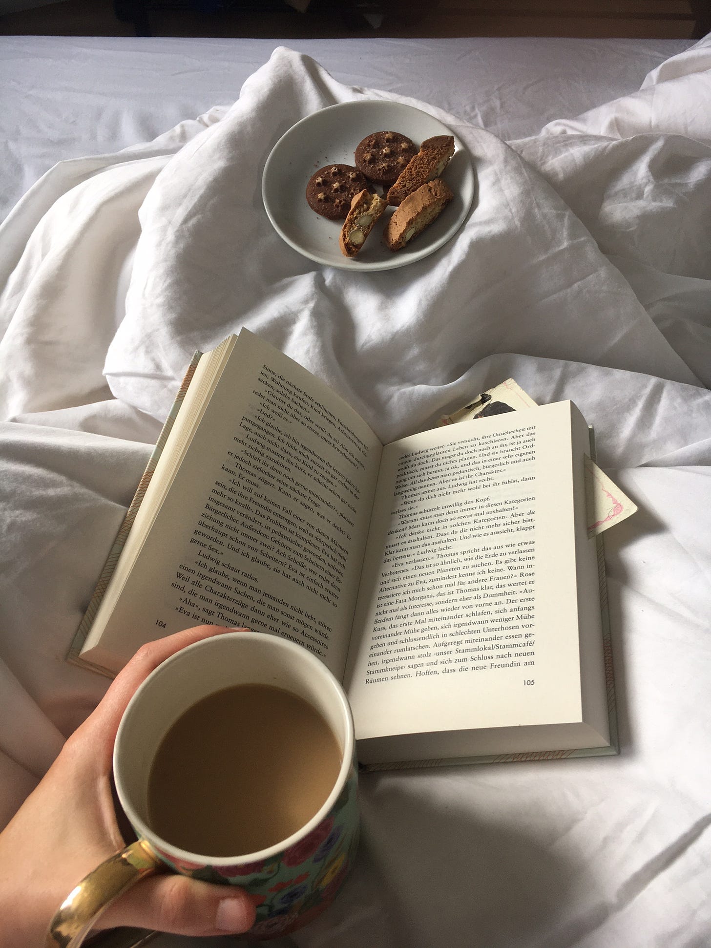Person liest im Bett mit Tasse Kaffee