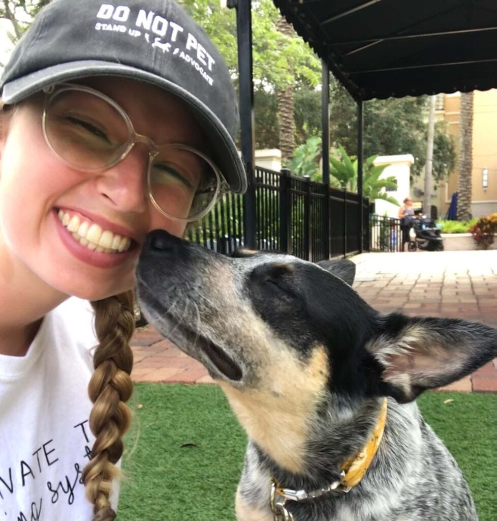 Scout the Australian cattle dog leans into her owners face as they pose for a selfie, with her owner wearing a hat that says Do Not Pet