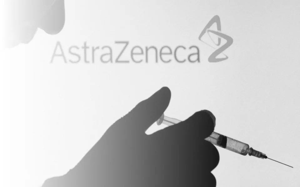 People pose with syringe with needle in front of displayed AstraZeneca