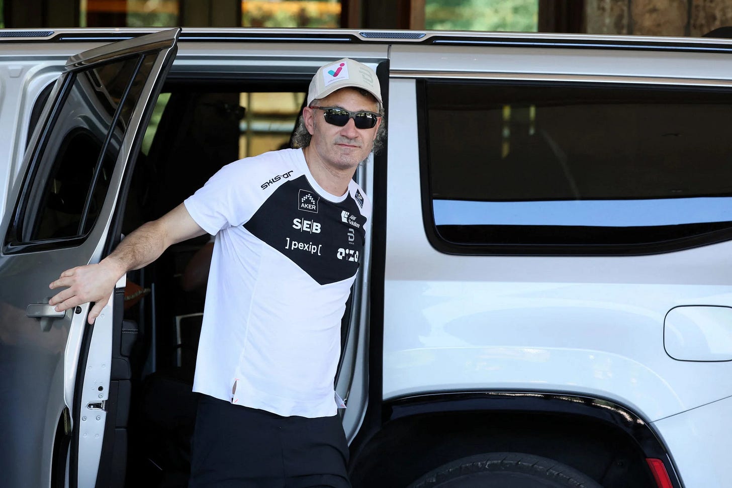 Alex Karp in a white jersey walking out of an SUV