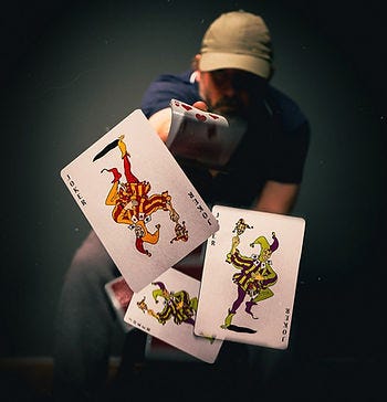 Dark background with a man in a baseball cap in the shadows, he is flicking out 3 joker cards to the foreground