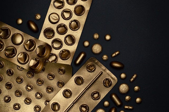 Blister packs of different kinds of pill, spraypainted gold, in front of a black background, an image in the public domain courtesy of Pixabay