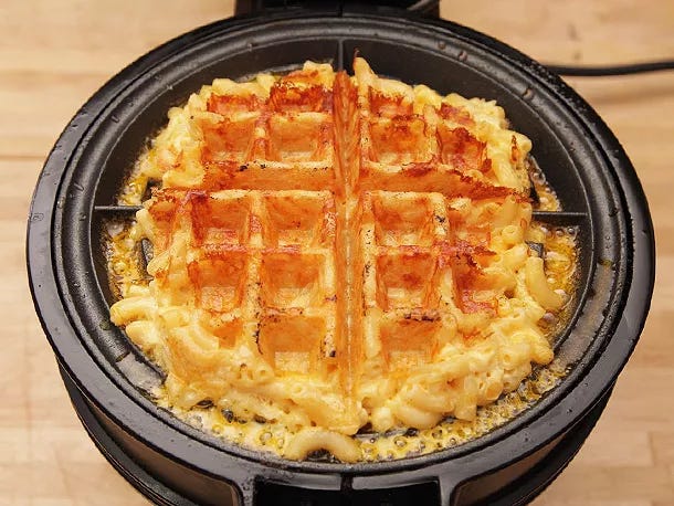 Waffled mac and cheese in a waffle iron with melted cheese oozing along the edges