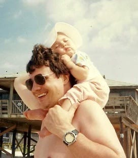 A person carrying a baby on his shoulders

Description automatically generated