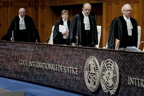 Four judges in black robes walk to their seats in front of a panel with the emblem of the International Court of Justice.