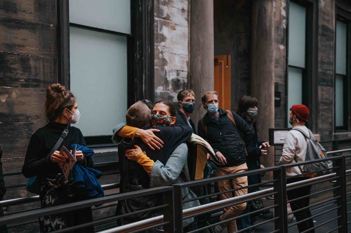 A handful of people wearing masks gather on the second floor of the CCA. Two are hugging each other.