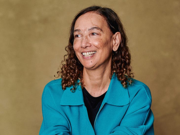 Jacqueline Crooks, with shoulder length curly brown hair and a  blue jacket