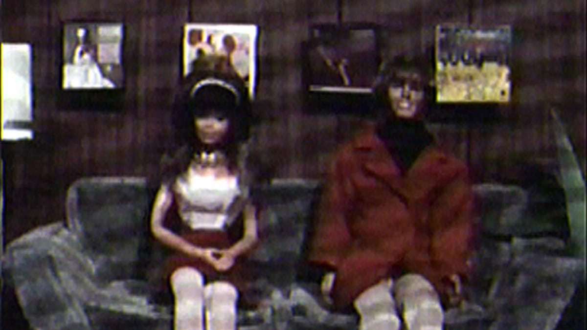 ID: A still from the 1988 film Superstar: The Karen Carpenter Story showing the Carpenter siblings as modified Barbie and Ken dolls sitting on an office couch
