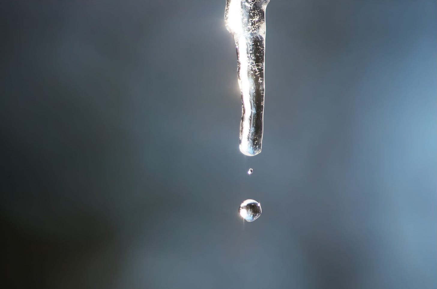 A perfectly round droplet falls from a brightly lit icicle.