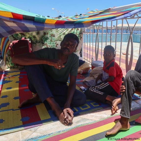 A Sudanese family, a father and likely two of his sons, wait at a camp
