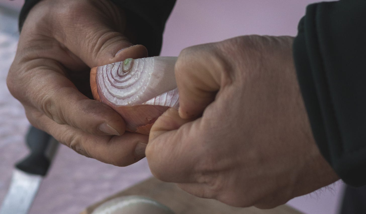 A pair of hands peel a half of an onion.