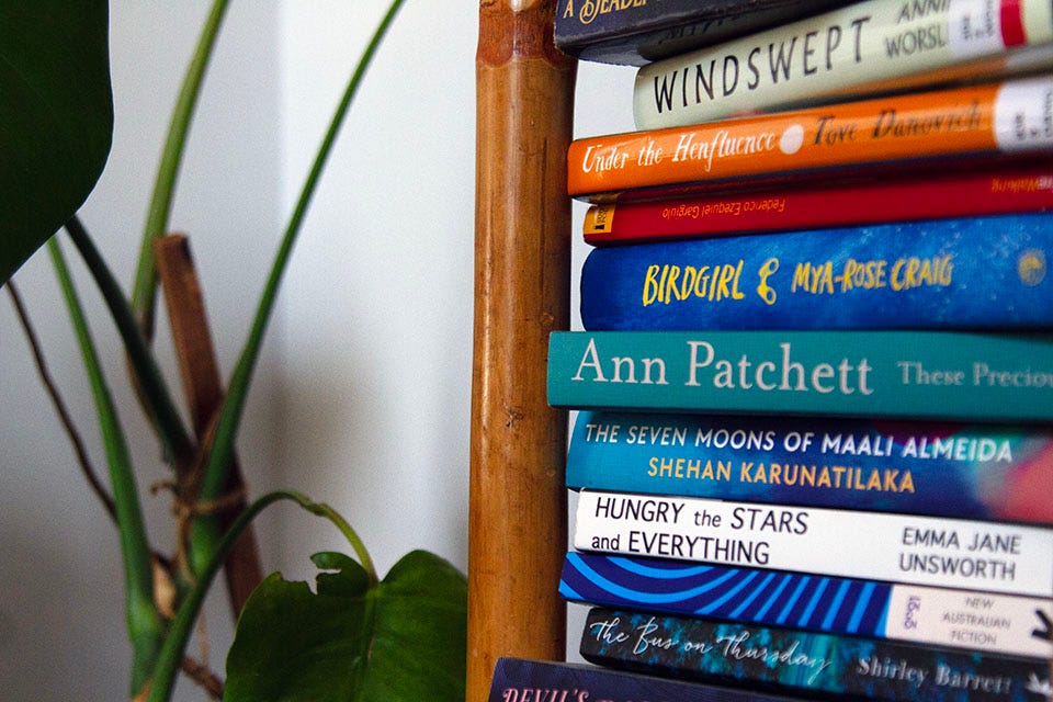 A stack of books on a shelf, next to a monstera houseplant.