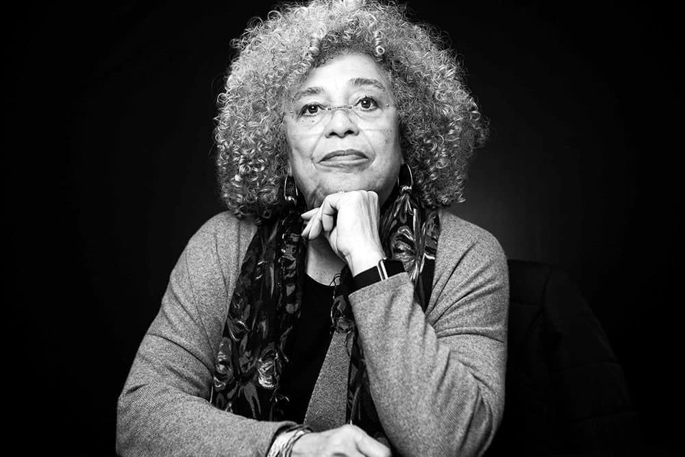 Portrait of Angela Davis inquisitively gazing at the camera with her chin resting against her hand