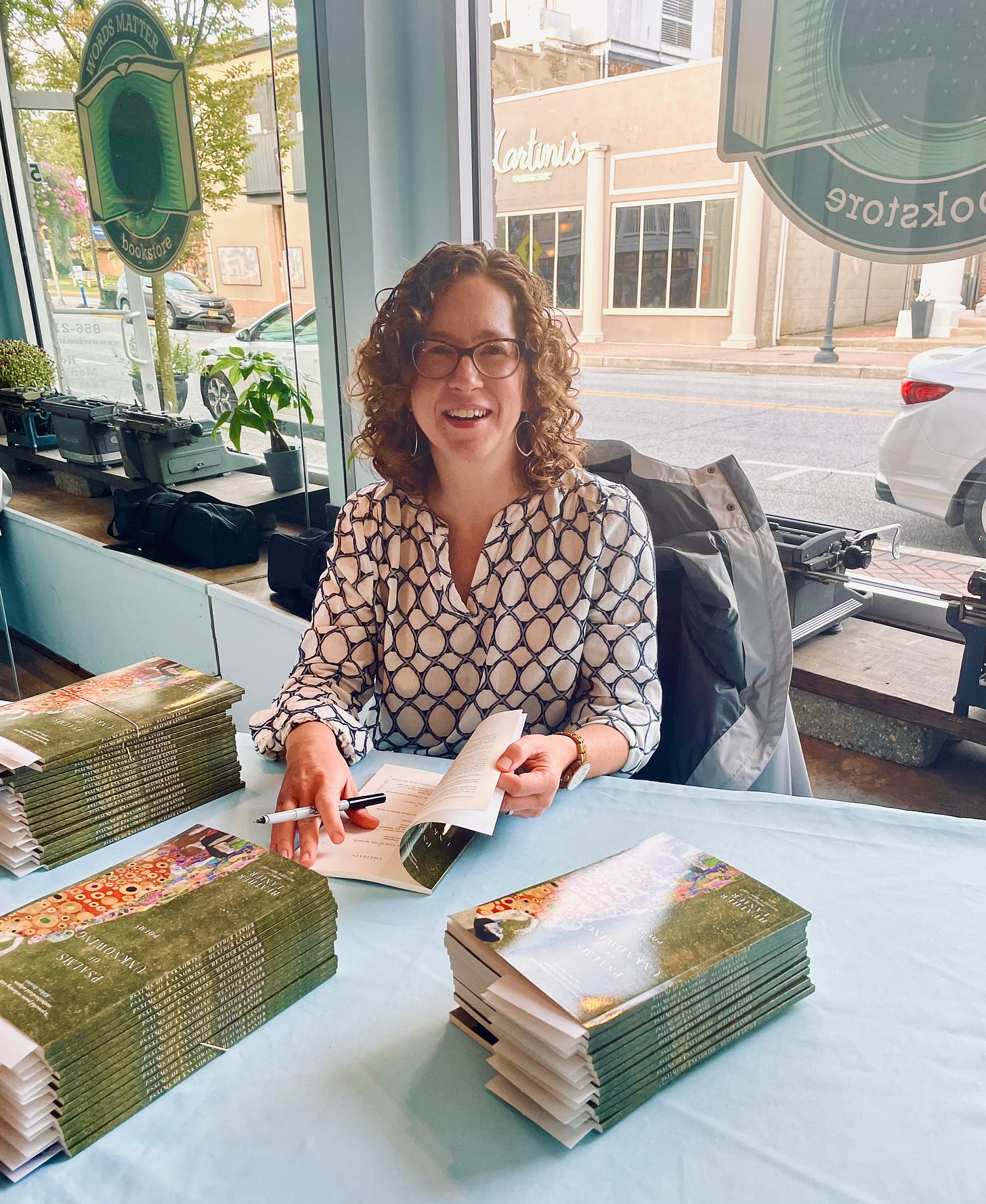 Author HEATHER LANIER signing books at a table. Behind her, a store front window facing a street.