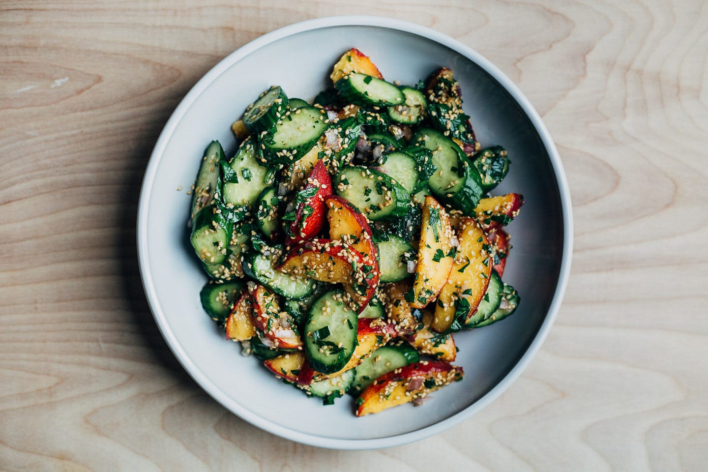 A bowl with a peach and cucumber salad topped with sesame seeds. 