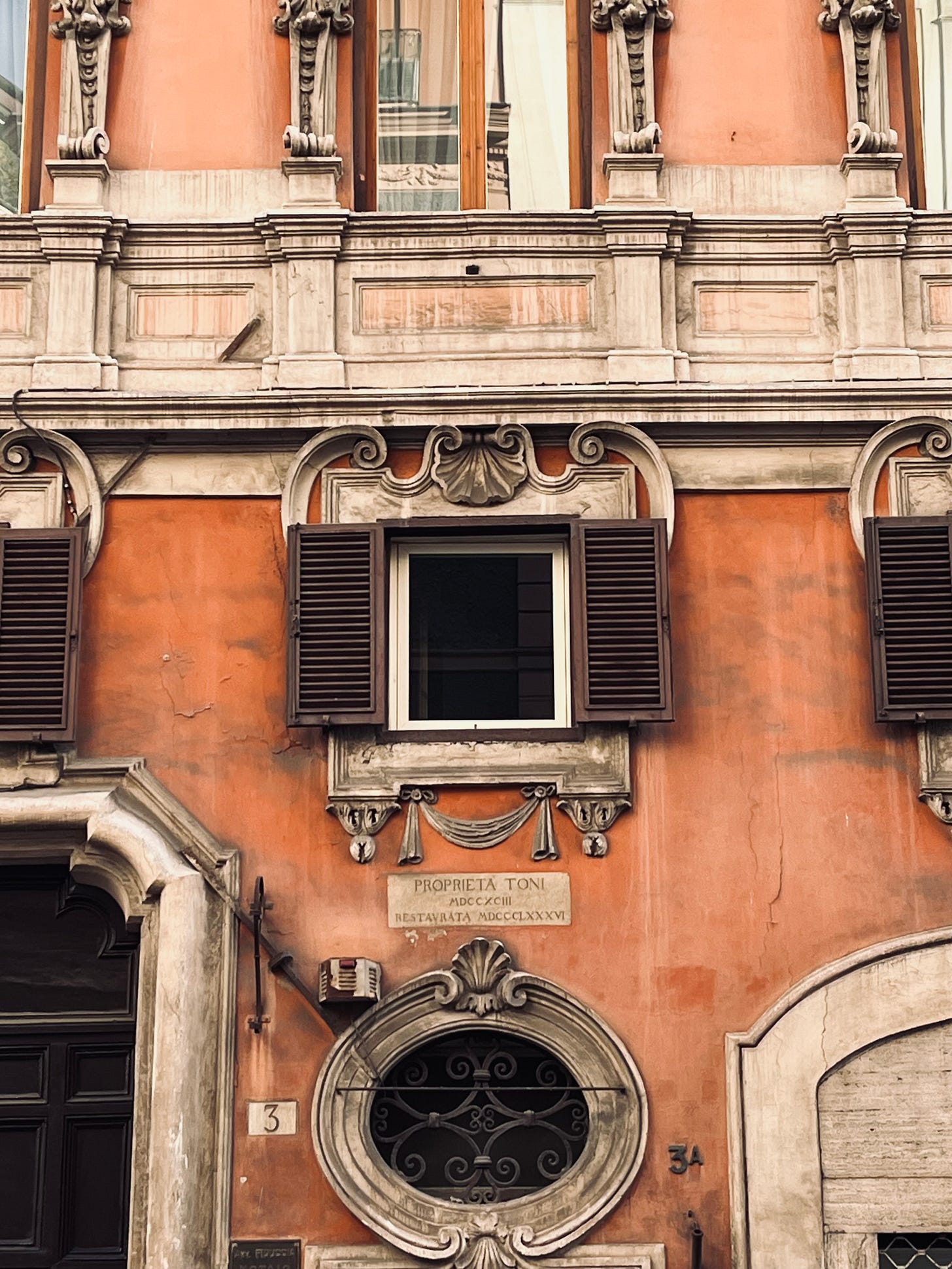 Ornate Roman building facade with terracotta walls, decorative stone details, and wooden shutters. Photo by Michelle Ciani.