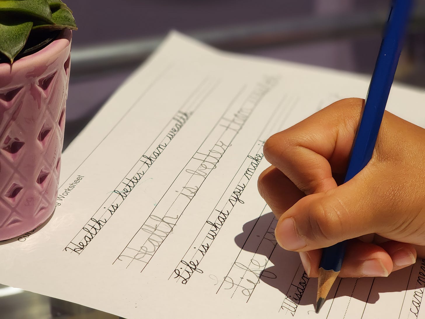 Image of a child's hand holding a pencil. The child is writing inspirational sentences in cursive. 