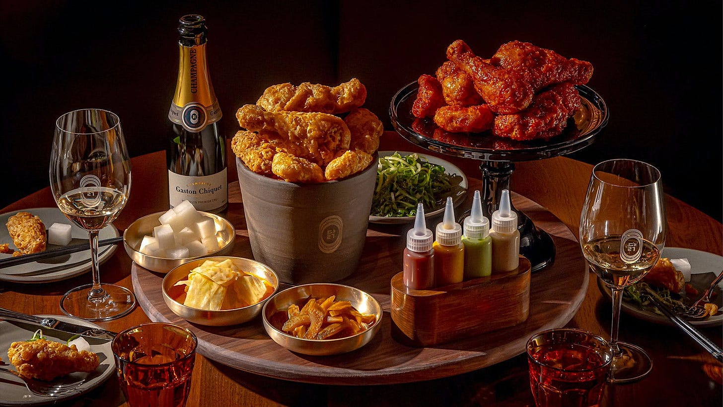 Table with buckets of Korean fried chicken, sauces, banchan side dishes, and glasses and bottles of Champage