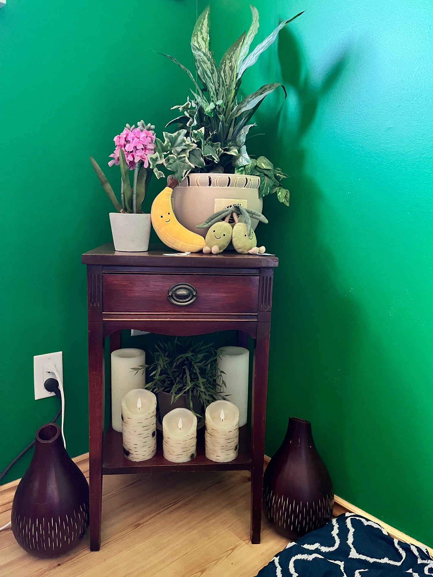 A brown nightstand holds fake plants, candles, a stuffed banana and stuffed olives