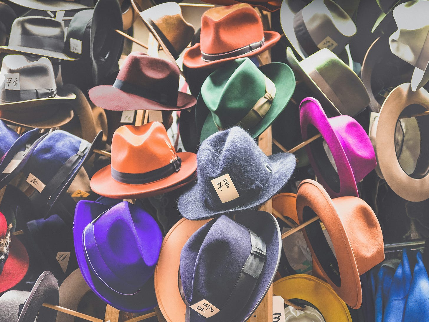 Many colorful fedora hats hanging on hooks, some have numbers on them