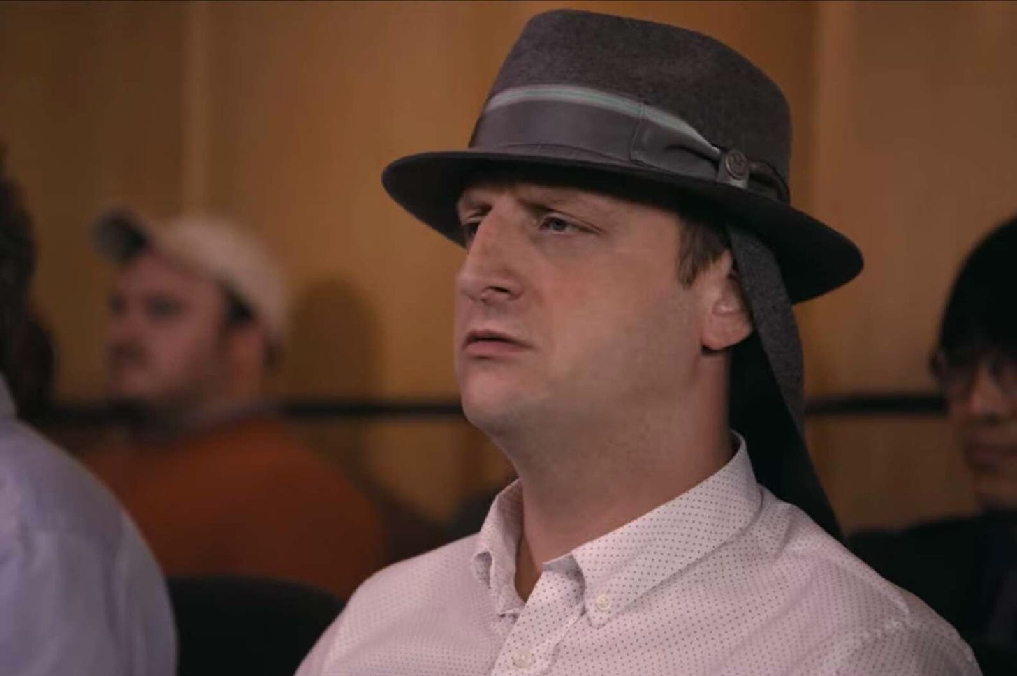 Tim Robinson wearing a very stupid hat with a flap on the back from I Think You Should Leave.
