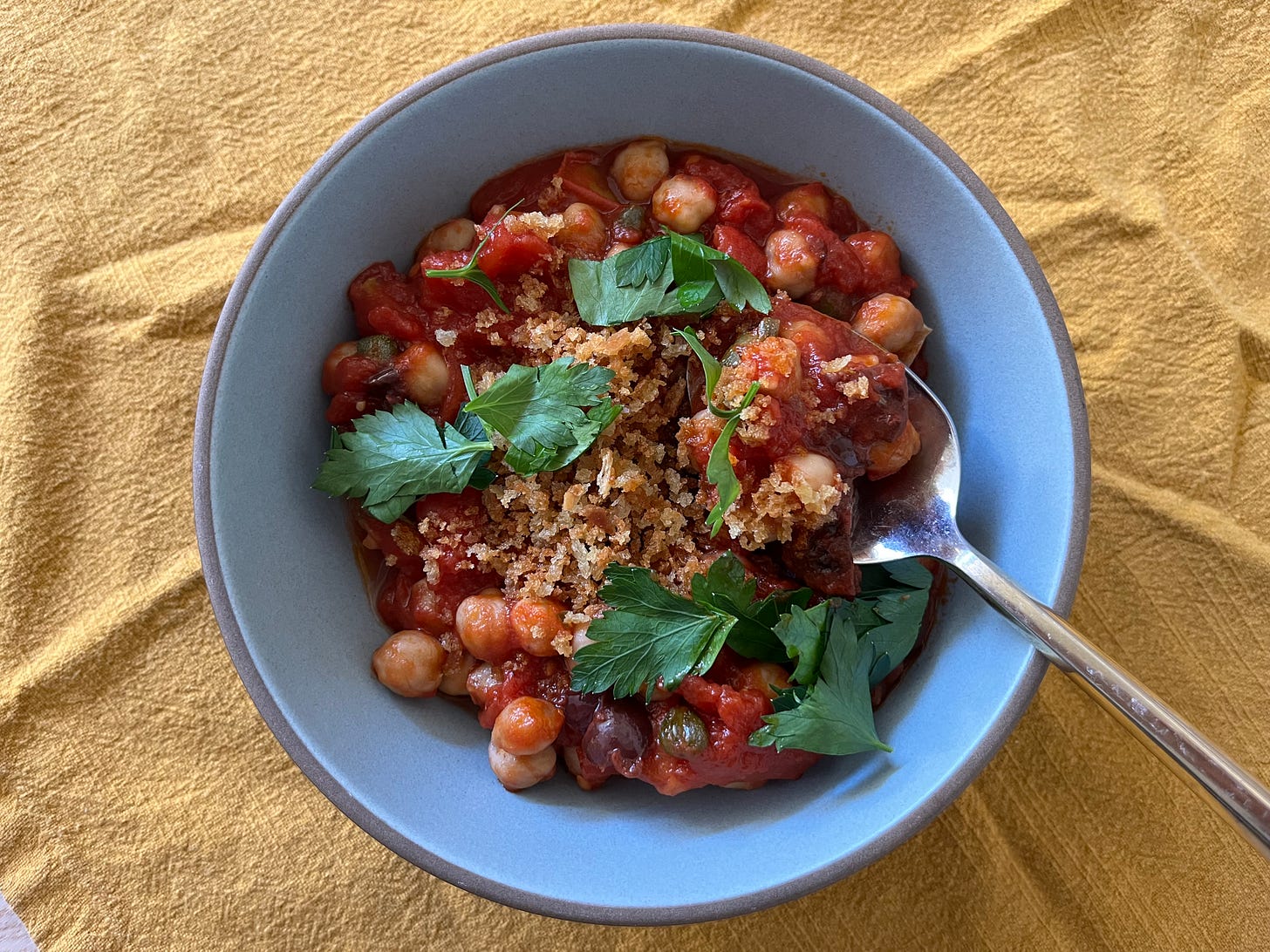 A bowl of chickpea puttanesca topped with toasted breadcrumbs and chopped parsley.