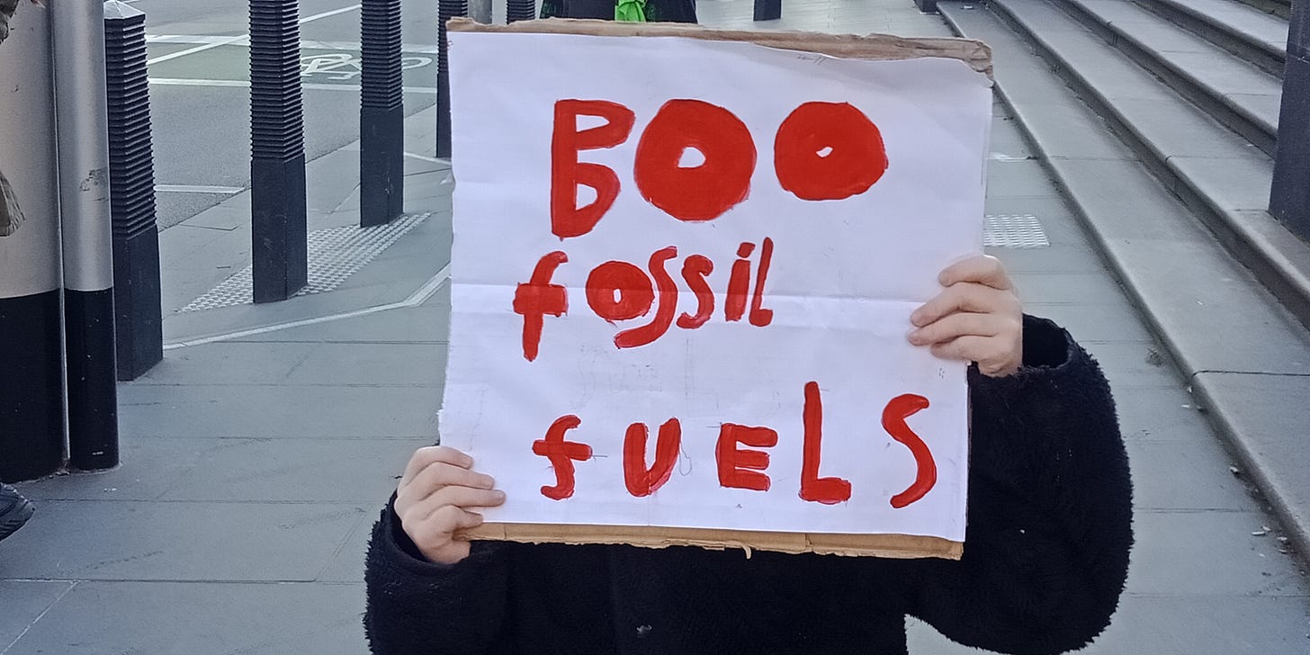 Child wearing black jumper holding sign covering race that reads Boo fossil fuels in child-like painted red letters