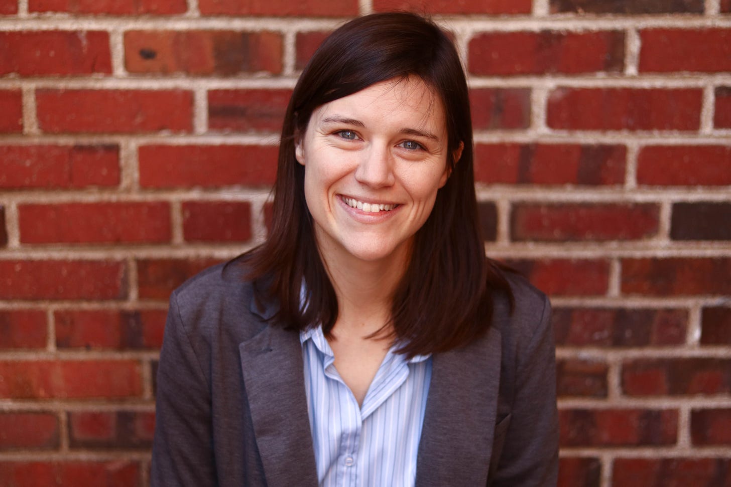 author photo of poet Alyse Knorr: a white woman with brown hair smiles in front of a red brick wall