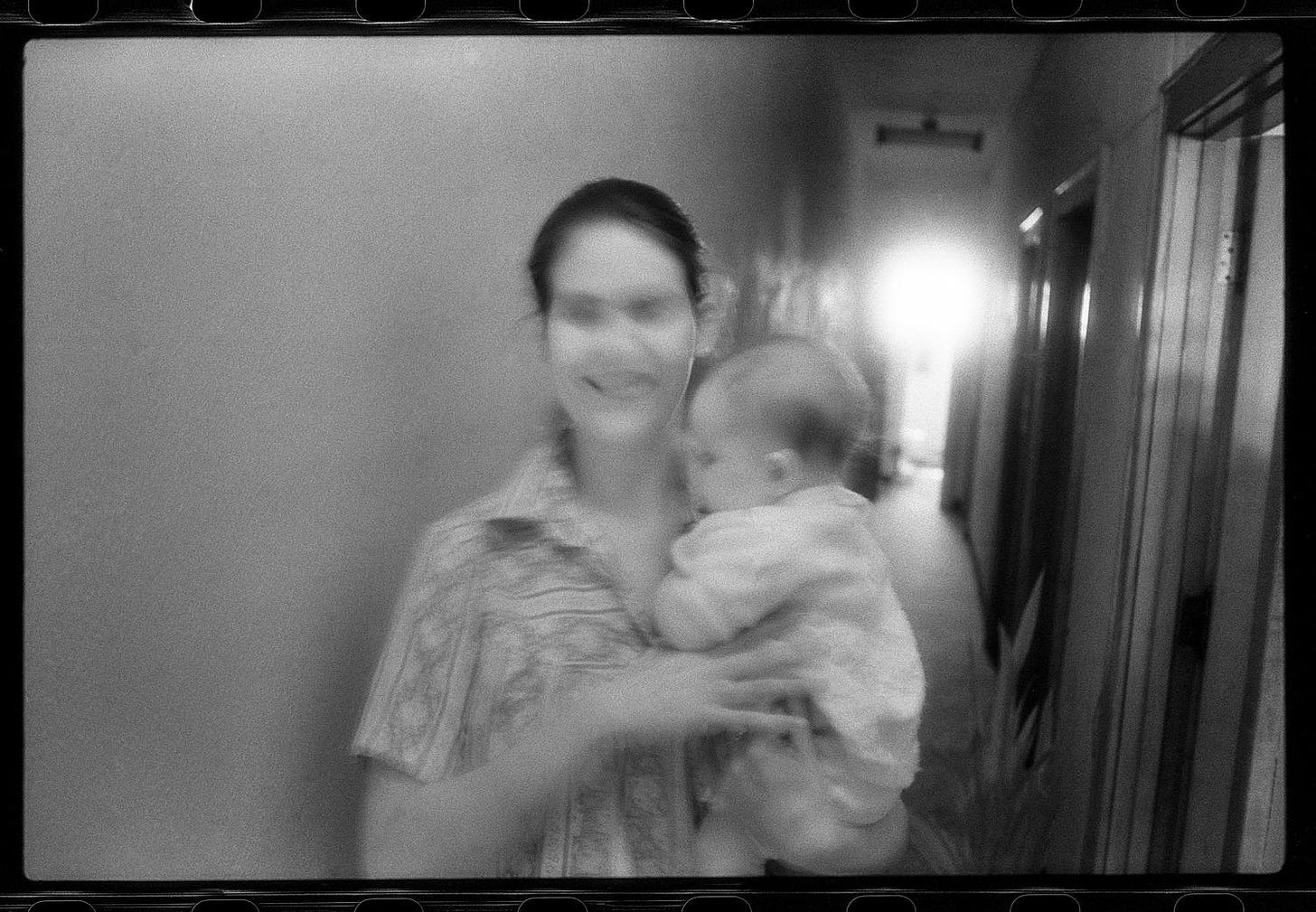large representation of [Woman standing in an apartment hallway holding a baby]. Side 1 of 1