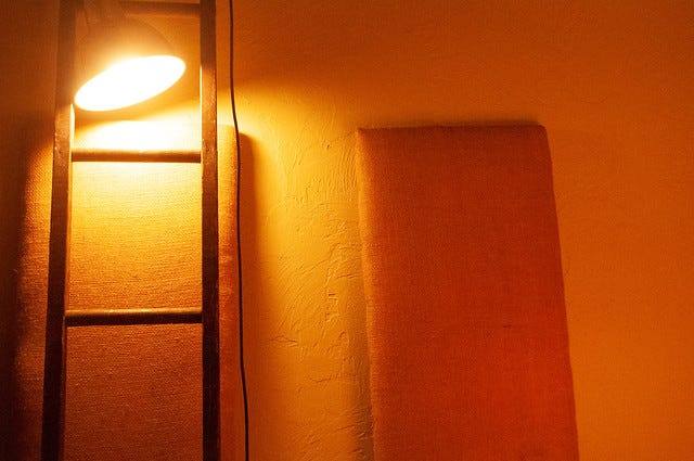 Photograph of a lamp hanging in front of a ladder and illuminating the wall behind it with an orangish glow